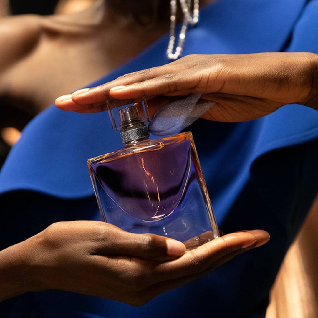 Mulher aplicando o perfume La Vie Est Belle, close-up do frasco e da pele